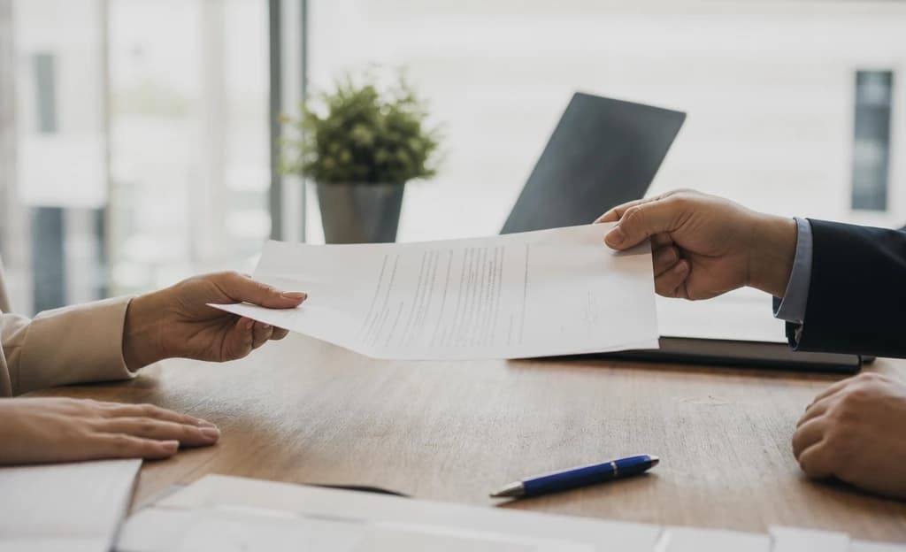 Document signé passant de main en main au-dessus d'un bureau, stylo et portable à proximité
